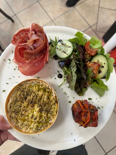 Assiette composée de prosciutto, de salade de concombre, de sauce cuite au four et de légumes rôtis, le tout servi dans un plat blanc.