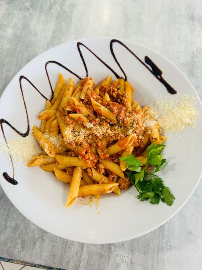 Pâtes penne à la sauce tomate servies sur une assiette blanche, garnies d'herbes, de fromage râpé et d'un filet de vinaigre balsamique.
