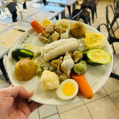 Une main tenant une assiette de légumes durs et d'œufs assortis dans un cadre de cafétéria.