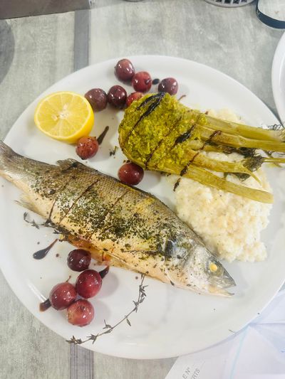Poisson servi avec du riz, du fenouil, du citron et des olives sur une assiette blanche.