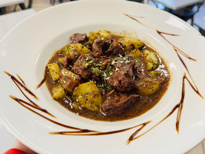 Ragoût de bœuf aux pommes de terre servi dans un bol blanc, garni d'herbes et d'un filet de vinaigre balsamique.