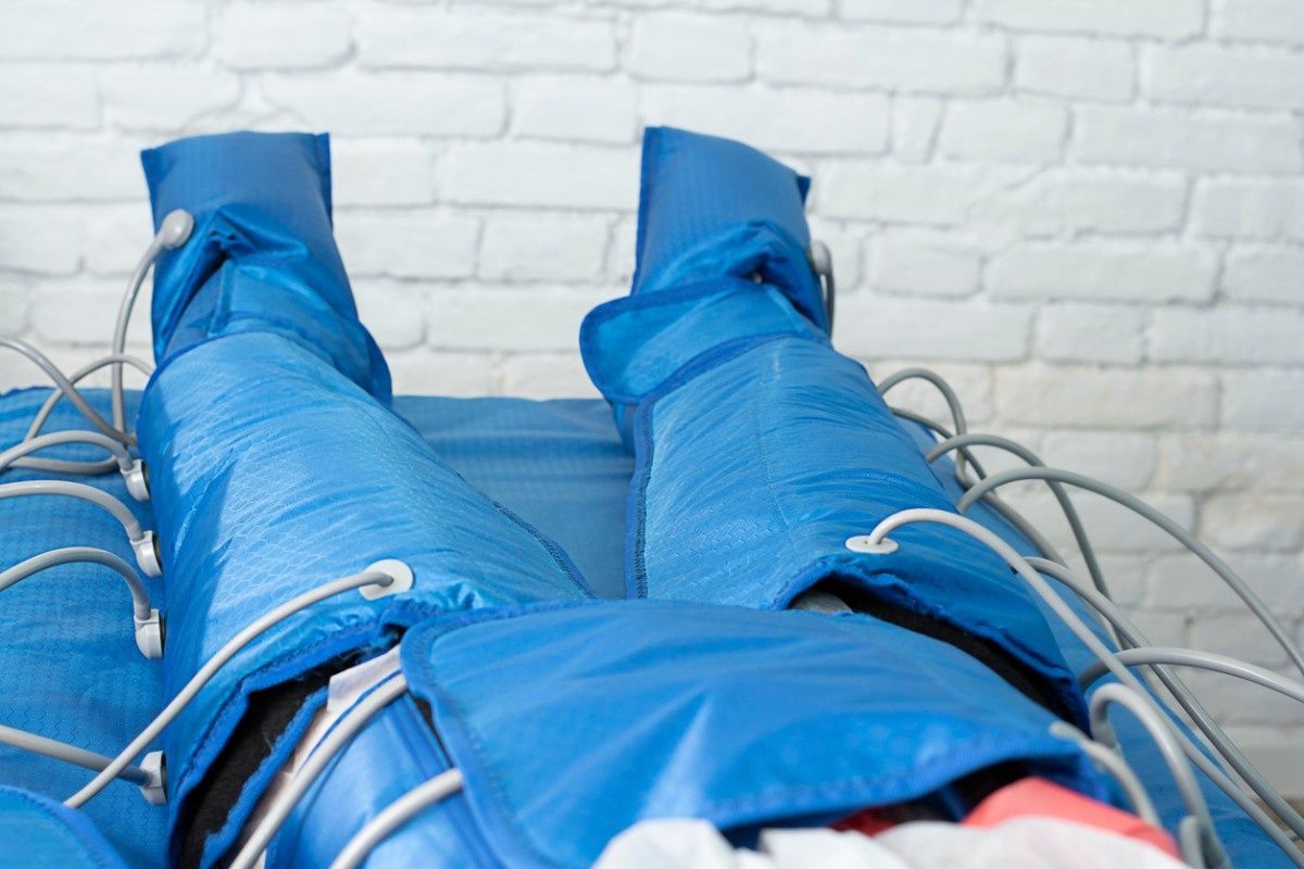 Botas de compresión azules envueltas alrededor de las piernas, colocadas sobre una superficie contra una pared de ladrillos blancos.