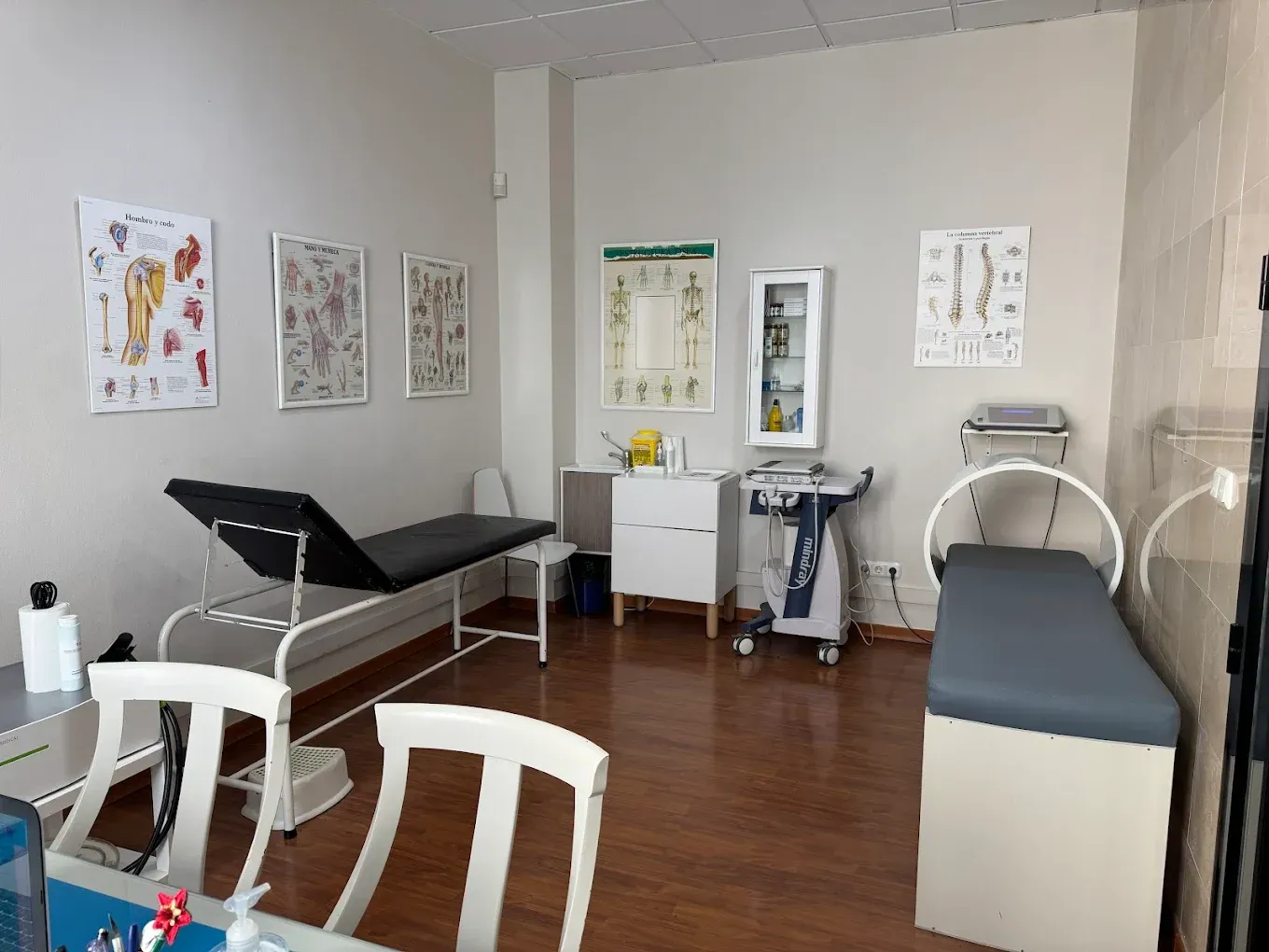 Sala de examen médico con mesas de examen, cuadros en la pared y equipo médico.