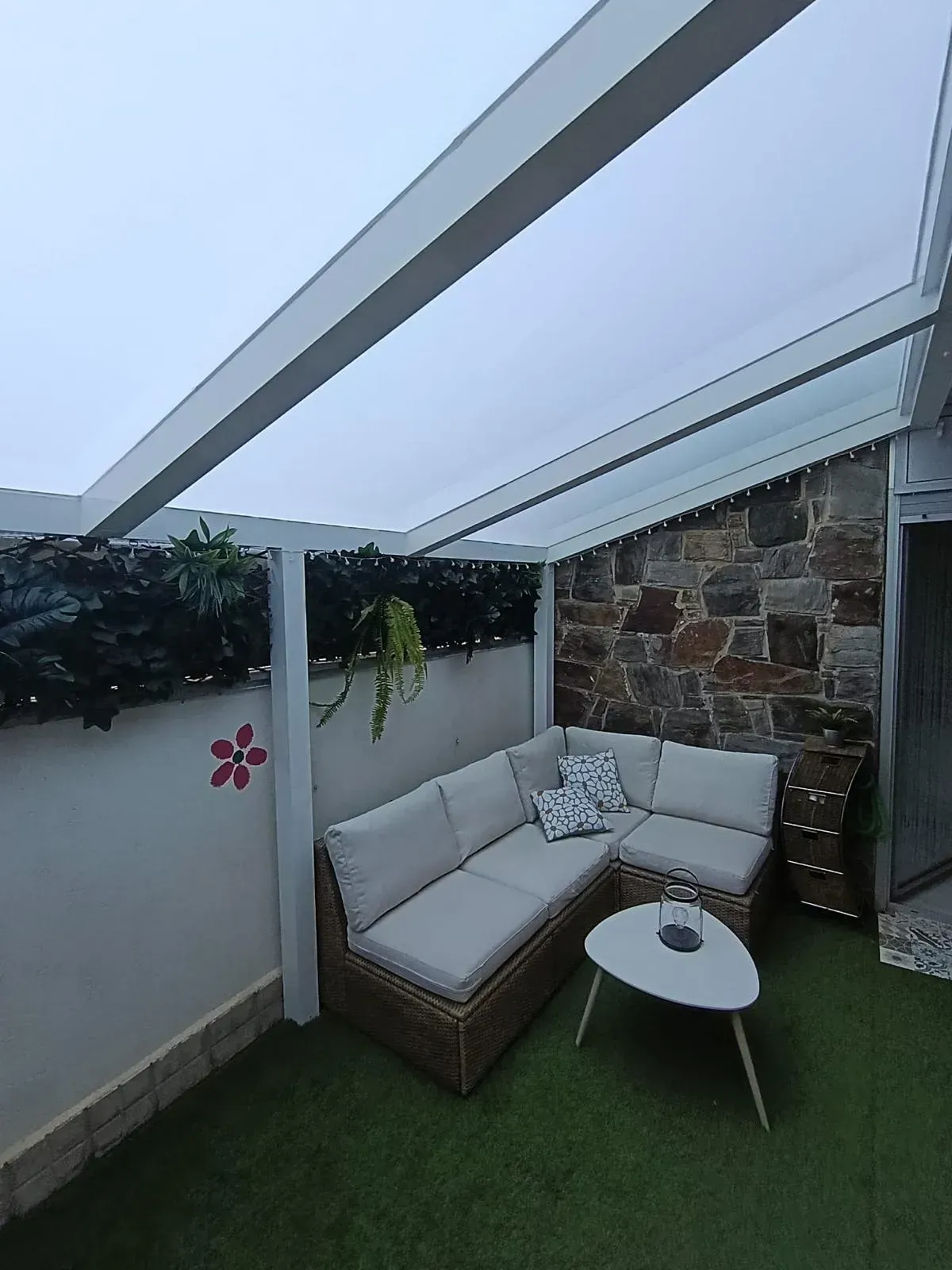 Zona de estar al aire libre con sofá beige, mesa pequeña y dosel.