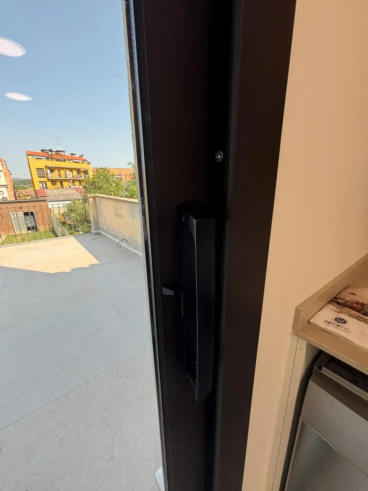 Manija de puerta negra en una puerta marrón oscuro, con vista a un tejado y al paisaje urbano.