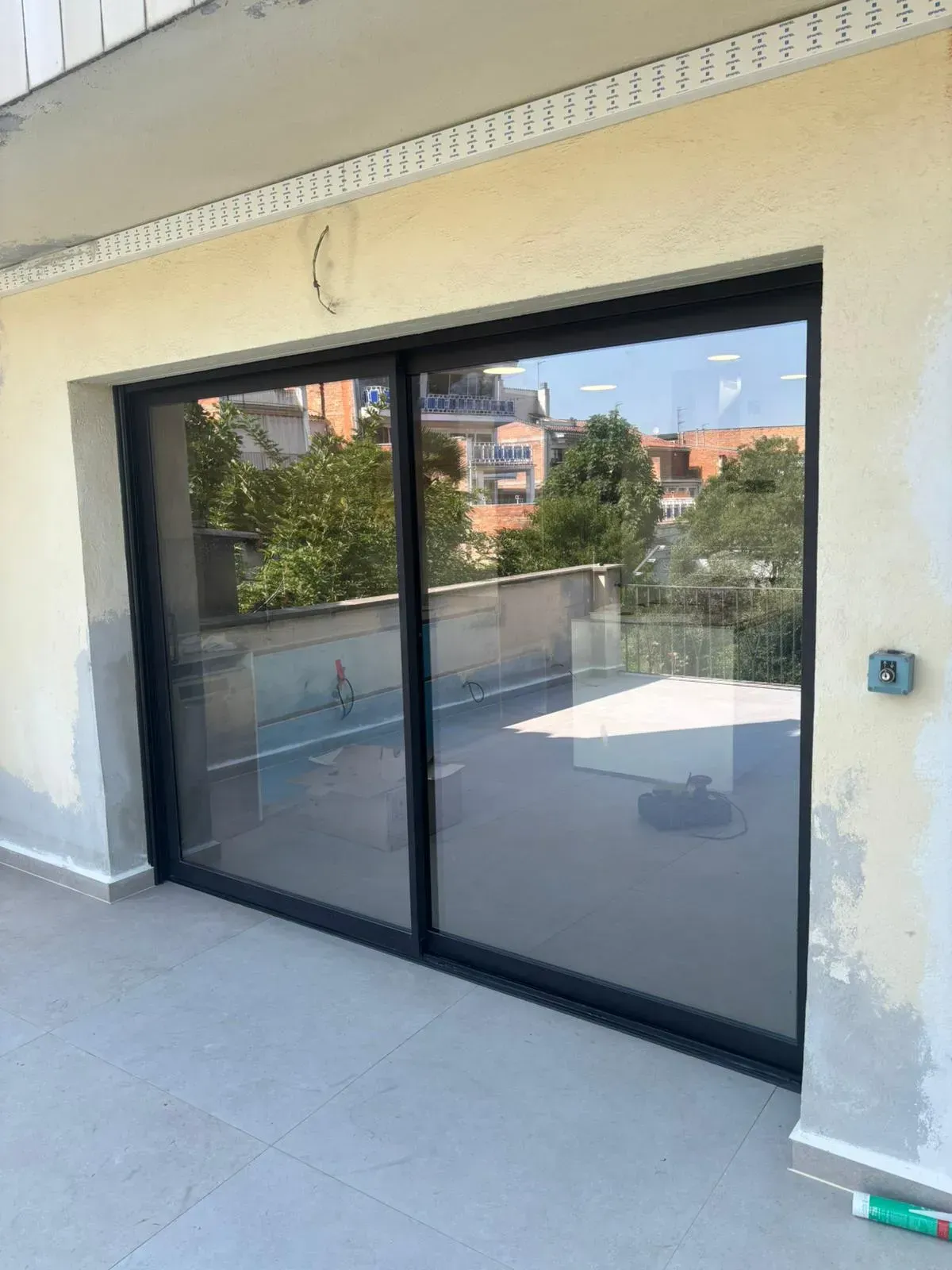 Puertas corredizas de vidrio con marcos negros en un balcón, que reflejan el entorno exterior.