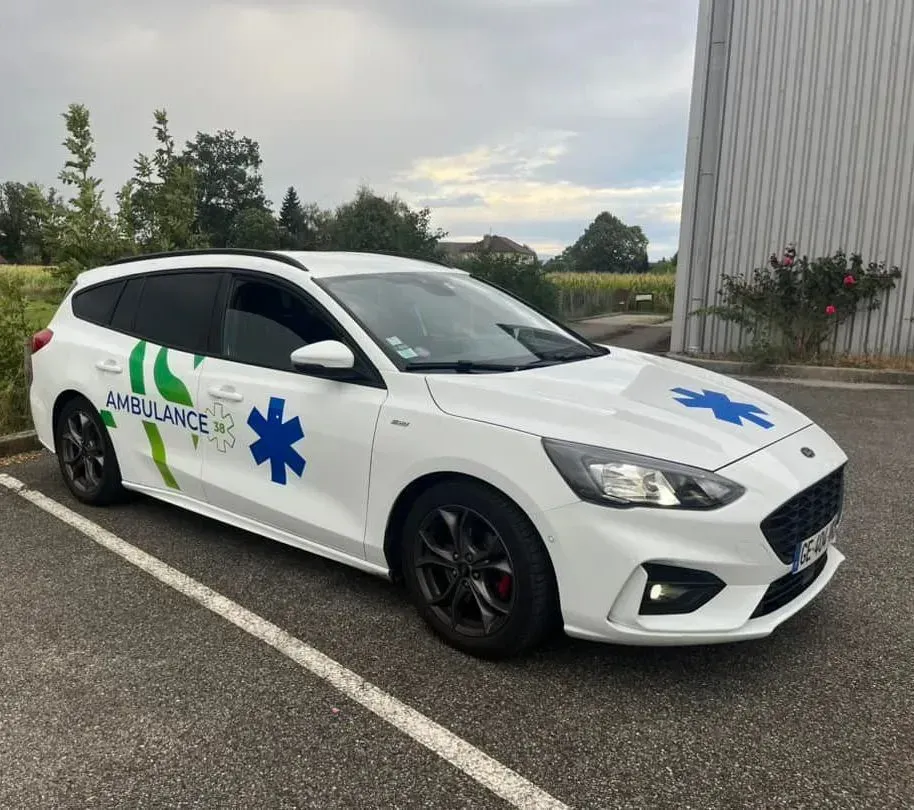 Une ambulance break blanche garée sur un stationnement goudronné, ornée d'étoiles de vie et de graphismes latéraux verts.