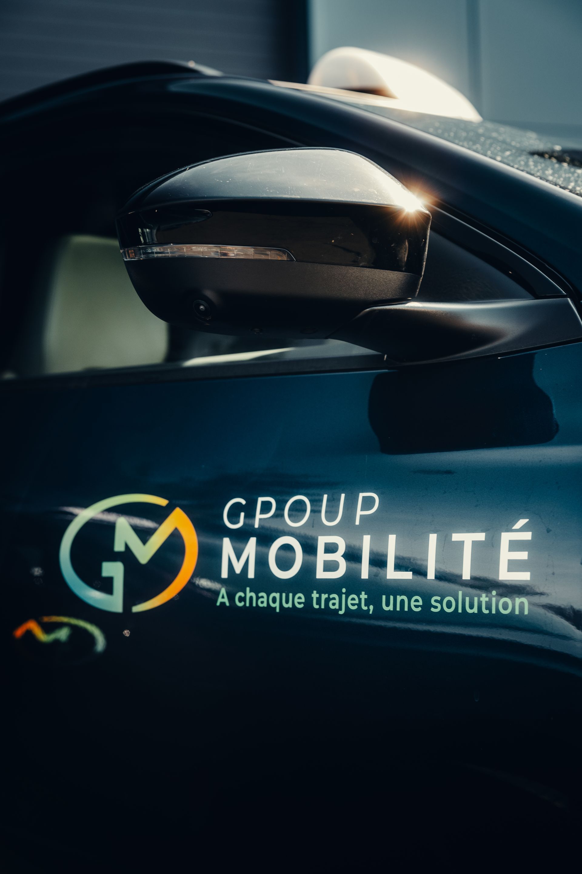 Logo “Group Mobilité” on a dark car side mirror, with the tagline “À chaque trajet, une solution.”