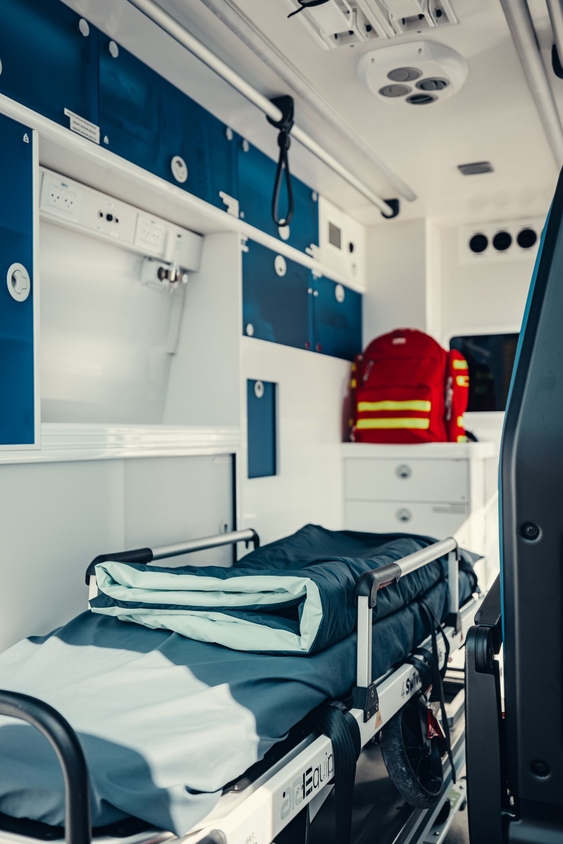 Intérieur d'un véhicule de transport médical avec une civière vide et du matériel d'urgence rouge.