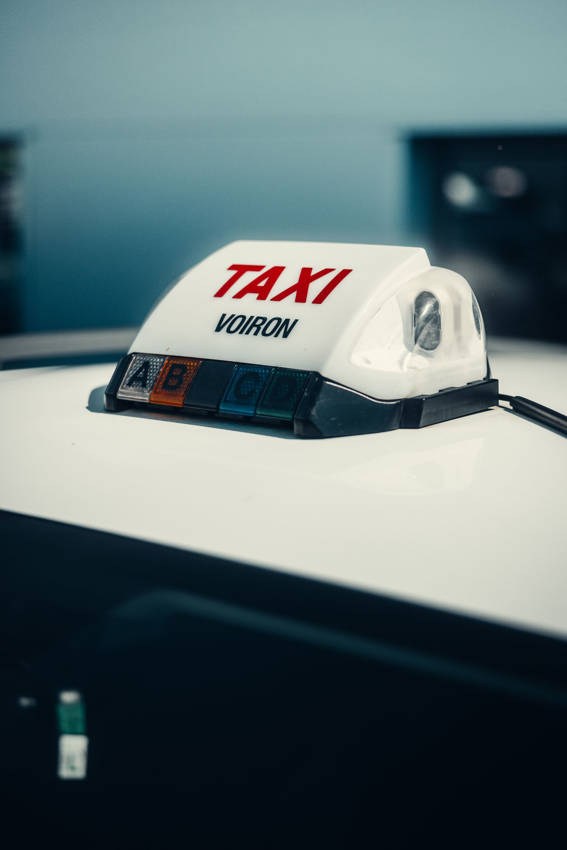 Panneau « Taxi » sur le toit d'une voiture, avec lettres rouges sur fond flou.