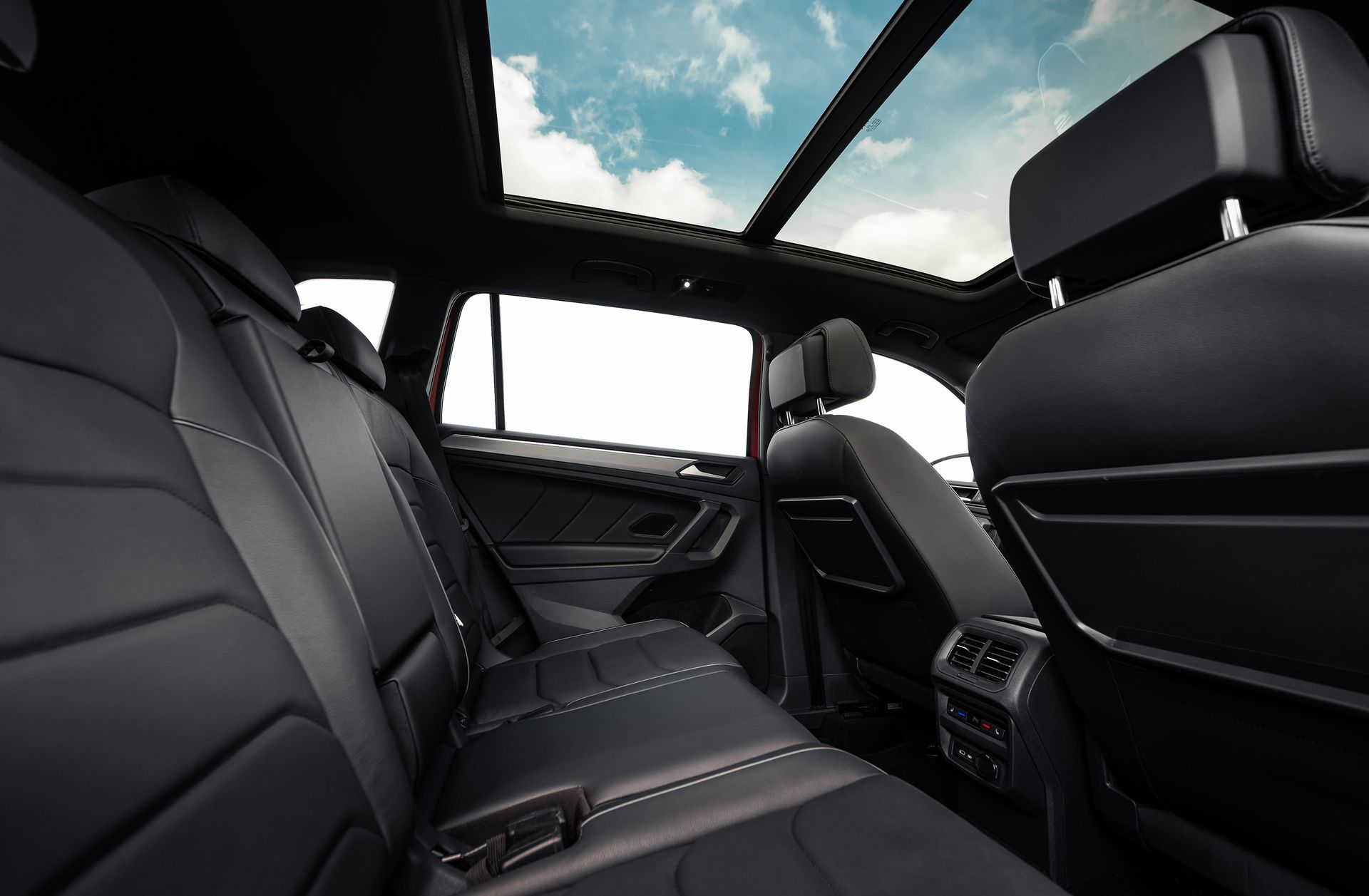Vue intérieure d'une voiture avec sièges en cuir noir, toit ouvrant panoramique laissant apparaître un ciel nuageux et aérateurs arrière.