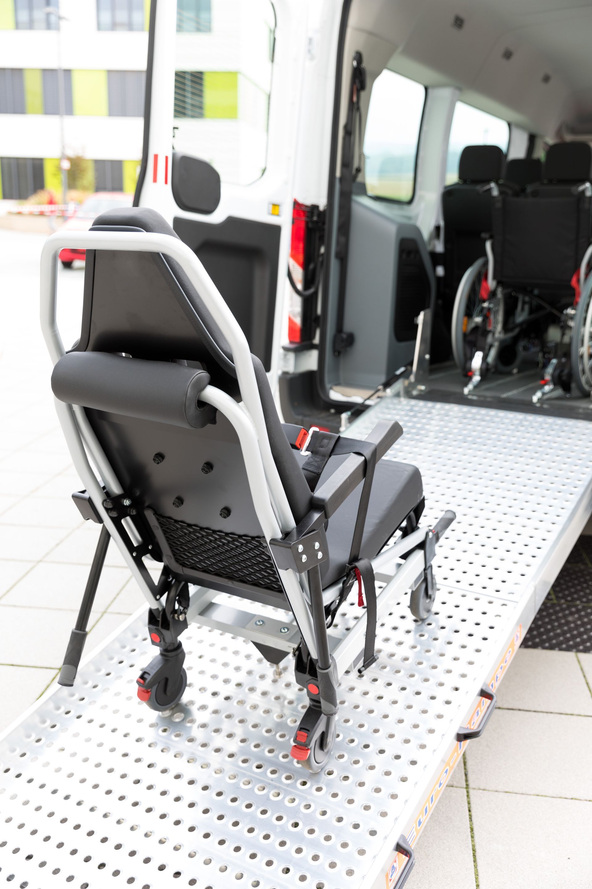 Un fauteuil de transport portable est installé sur une rampe abaissée à l'arrière d'une camionnette accessible, un fauteuil roulant se trouvant à l'intérieur du véhicule.