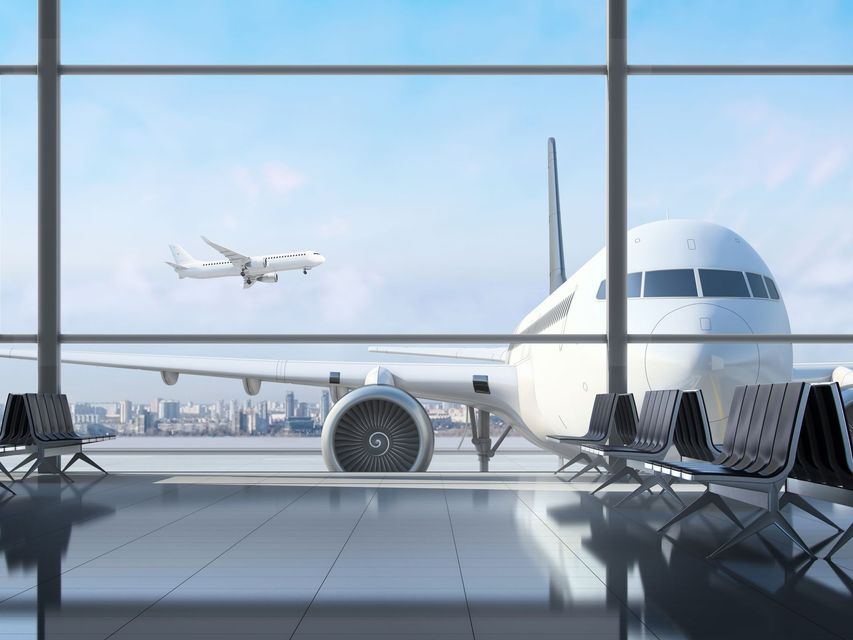 Vue depuis un terminal d'aéroport montrant un gros avion stationné sur le tarmac et un avion plus petit volant au loin.