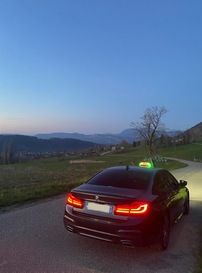 Un taxi noir stationné sur une route de campagne tranquille au crépuscule, avec des montagnes au loin sous un ciel bleu.