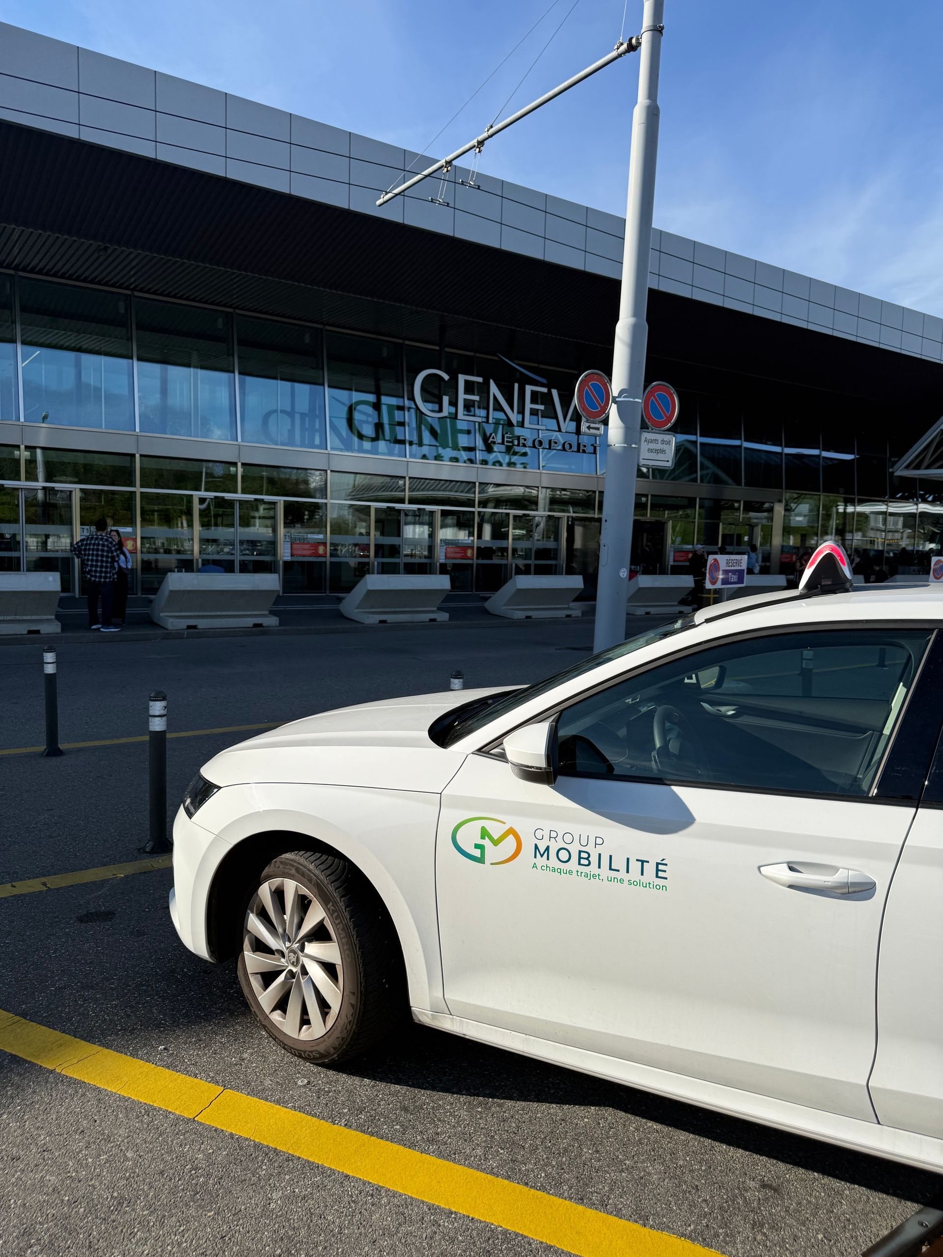 Voiture blanche garée devant le terminal de l'aéroport de Genève par une journée ensoleillée