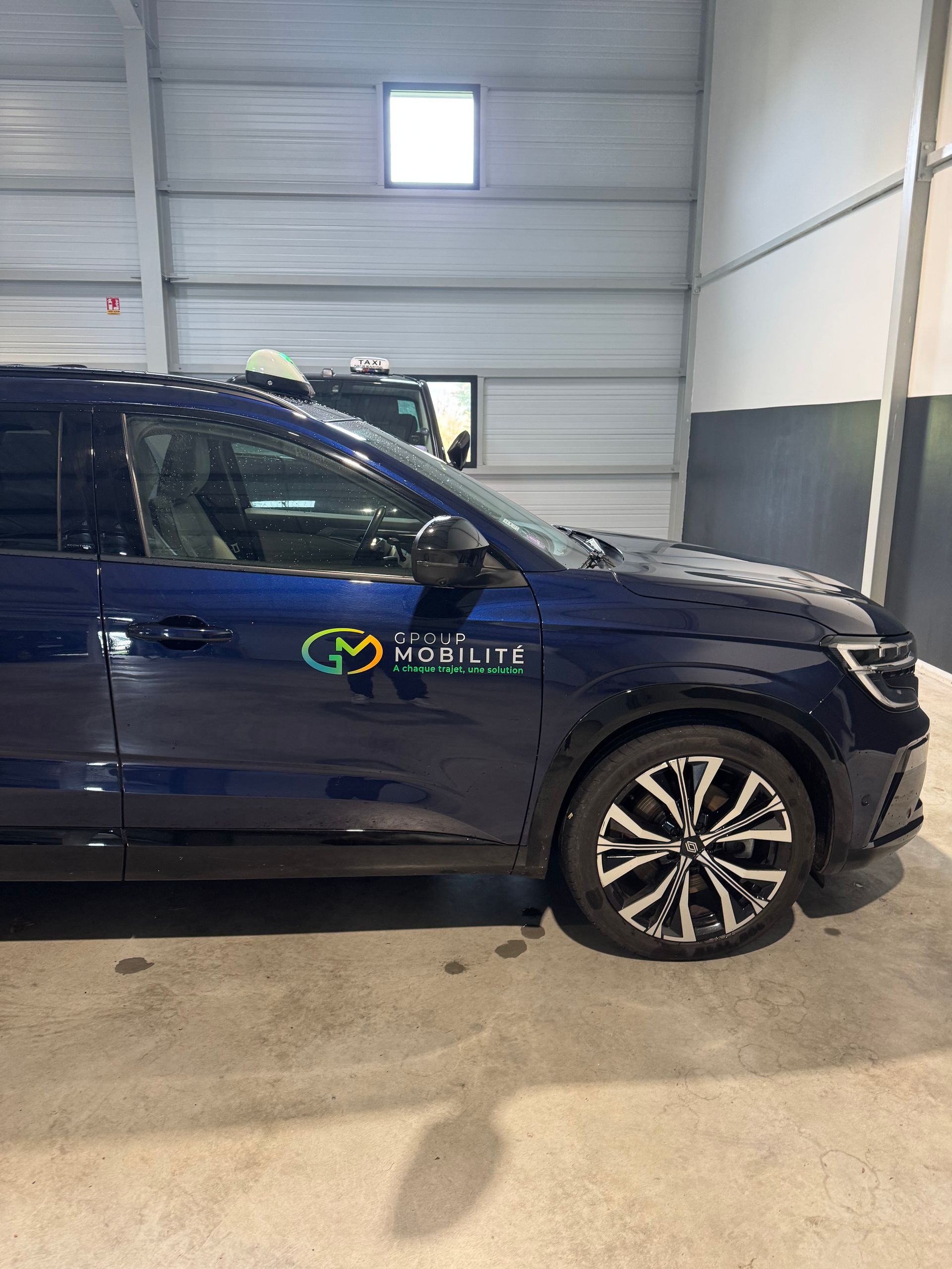 Un SUV bleu foncé avec un logo sur la portière côté conducteur est garé à l'intérieur d'un entrepôt aux murs métalliques.
