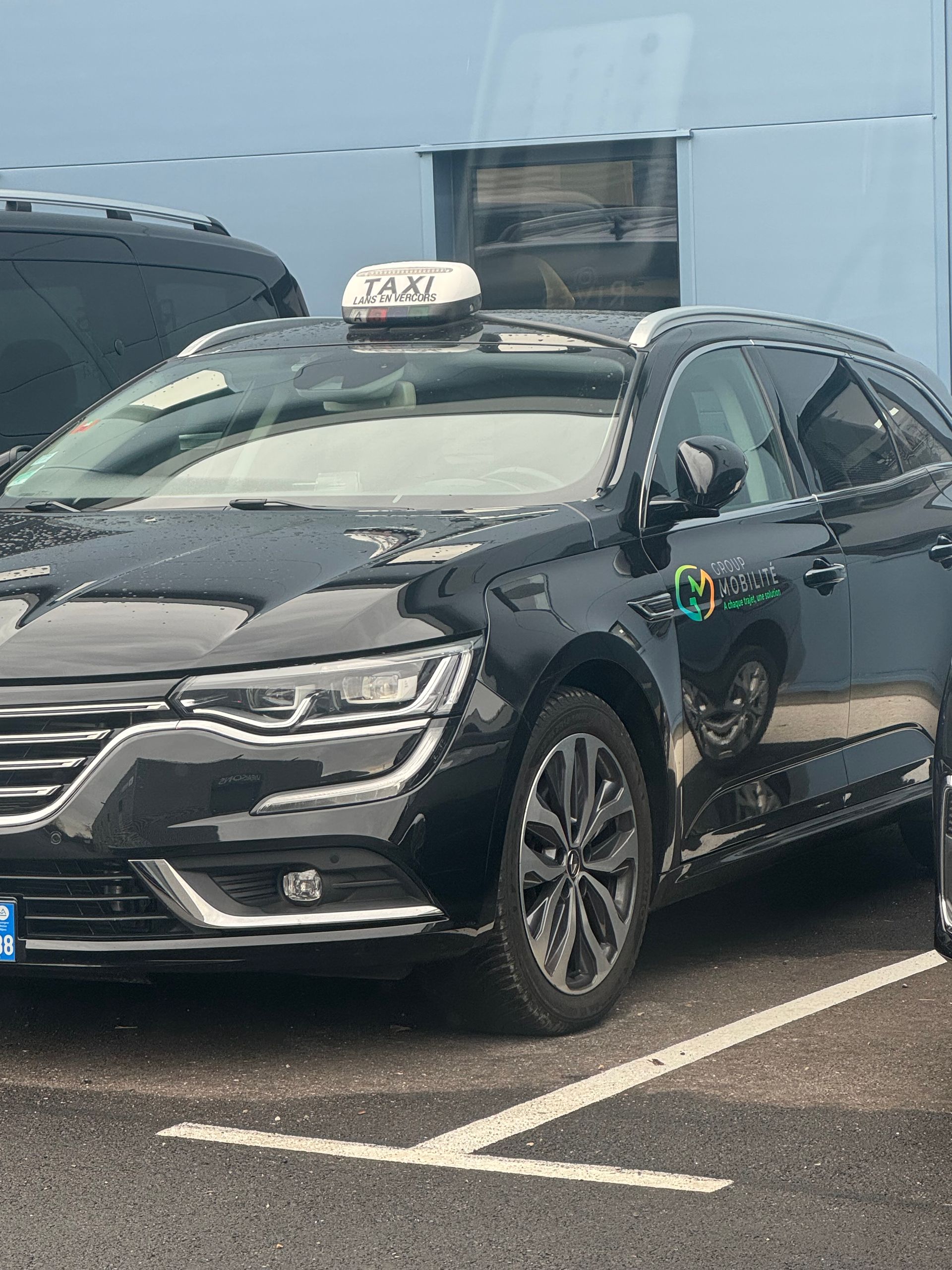 Un taxi noir garé sur un stationnement extérieur, montrant son profil avant côté passager et son panneau de taxi sur le toit.
