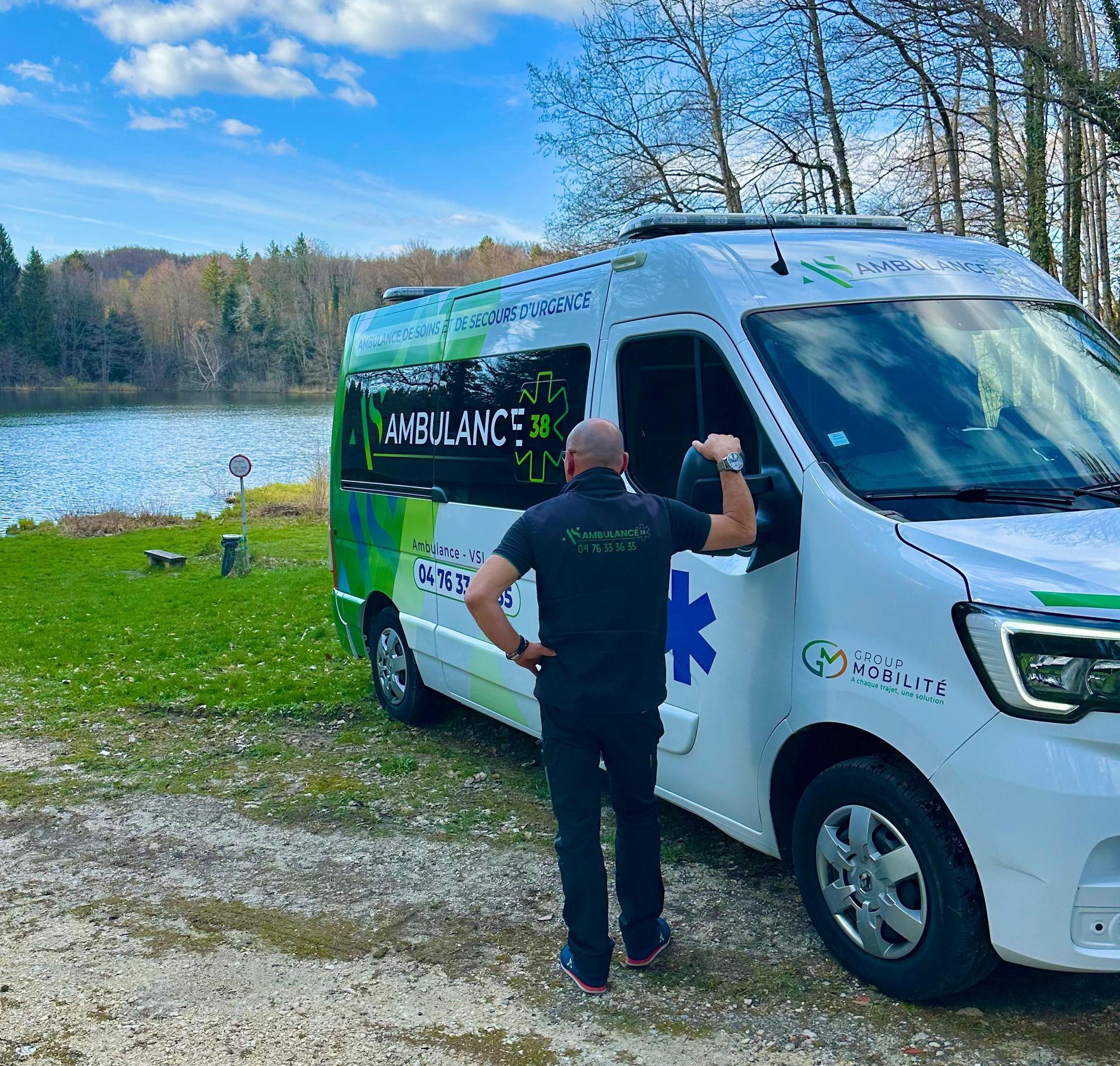Une ambulance près d'un lac, une personne se tenant à côté, sur une rive herbeuse.