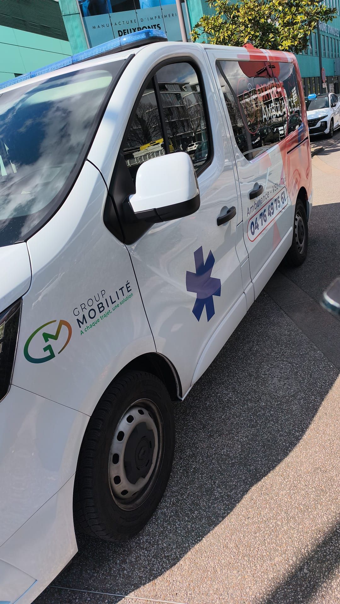 Une camionnette blanche ornée de logos du secteur de la santé était garée dans une rue ensoleillée, parmi d'autres voitures.