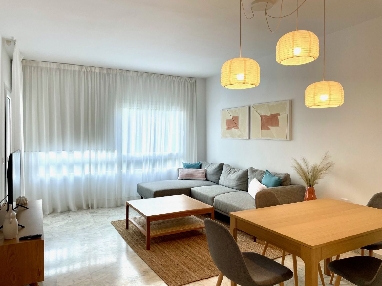 Sala de estar con un sofá seccional, una mesa de centro de madera y una mesa de comedor. Tres lámparas colgantes cuelgan encima.