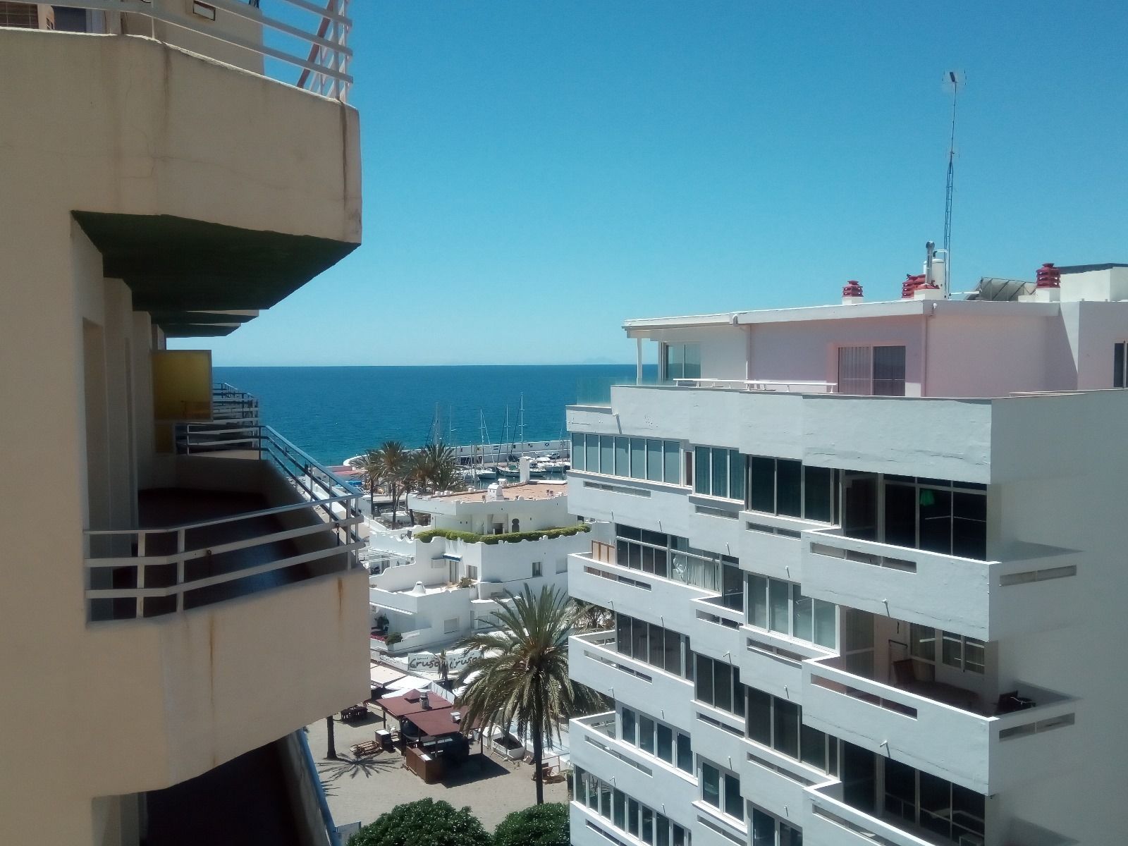 Vista del océano y edificios con balcones bajo un cielo azul brillante.