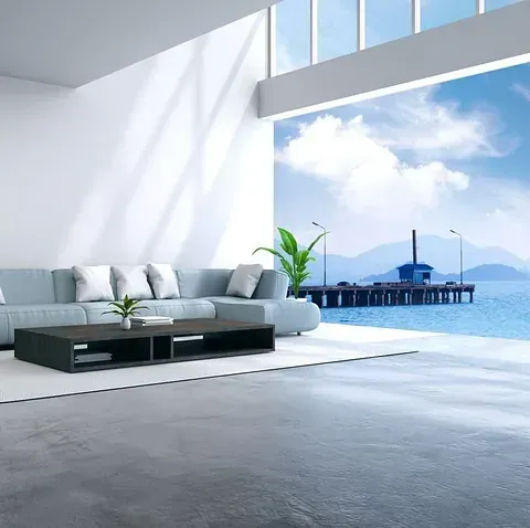 Una sala de estar moderna y luminosa con un gran ventanal con vistas al muelle y al mar. Incluye un sofá seccional gris y una mesa de centro negra.