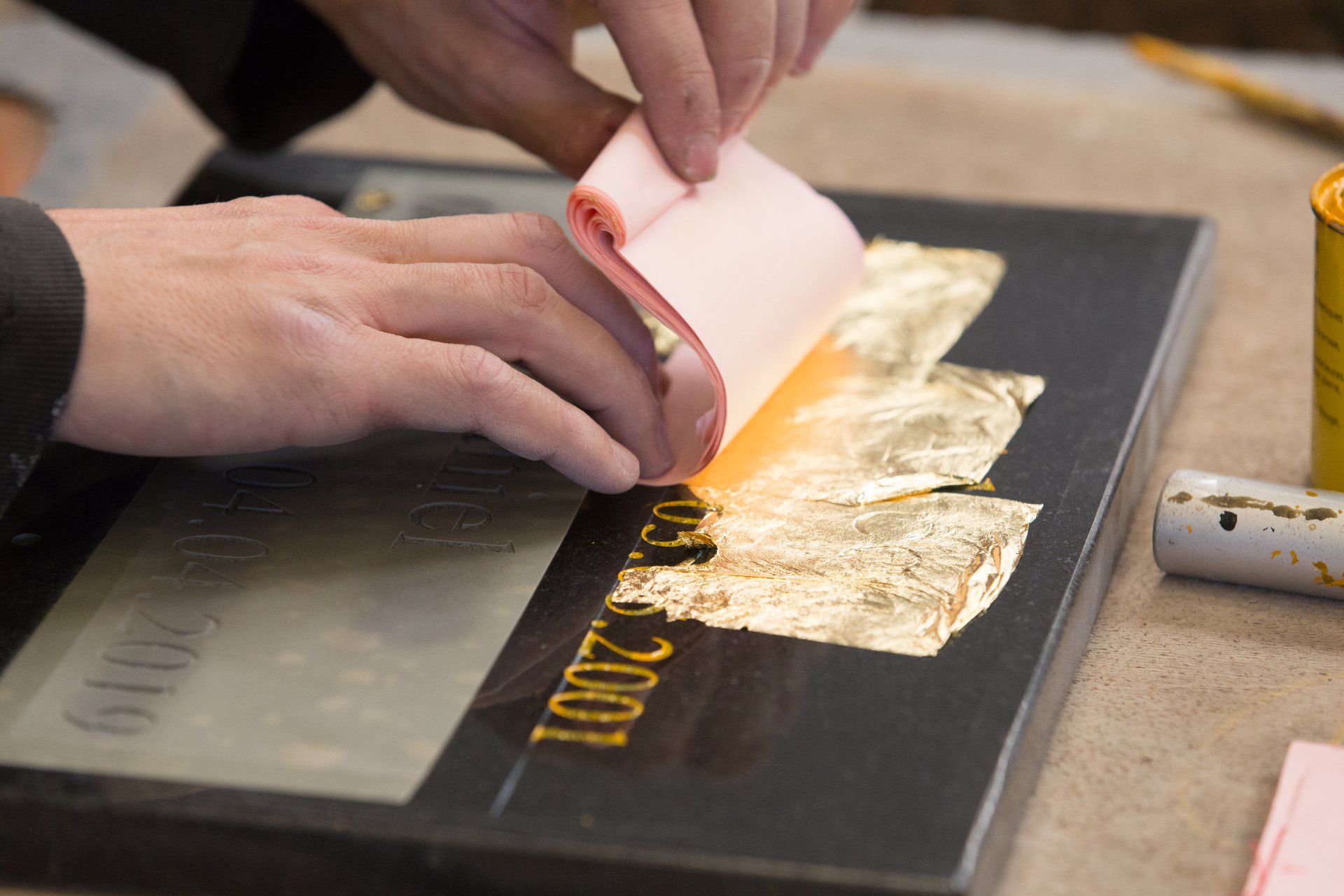 Des mains appliquent des feuilles d'or sur une gravure