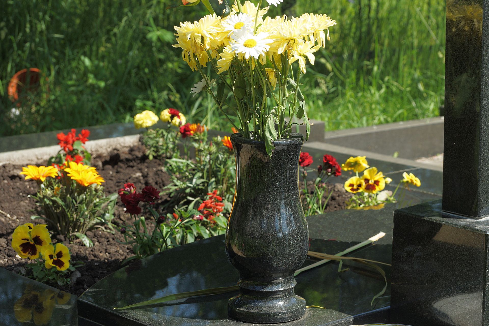 Vase contenant des fleurs près d'une plaque en marbre d'une tombe végétalisée