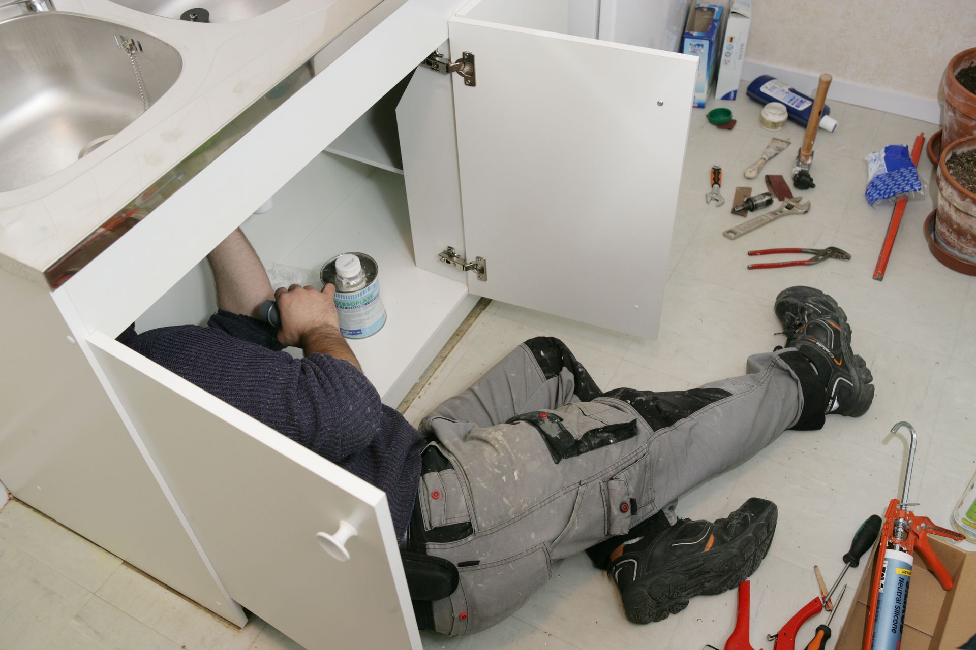 Un plombier réalise des travaux sous un évier.