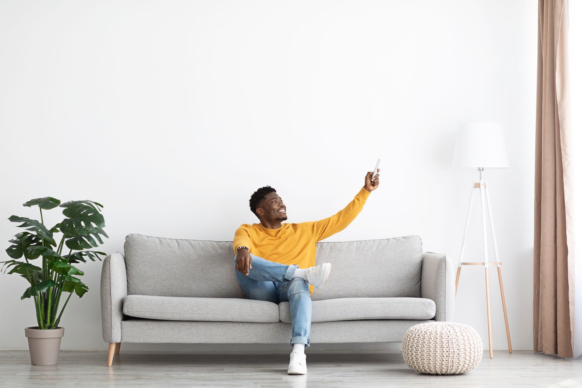 Un homme sur un canapé tient une télécommande de climatisation.