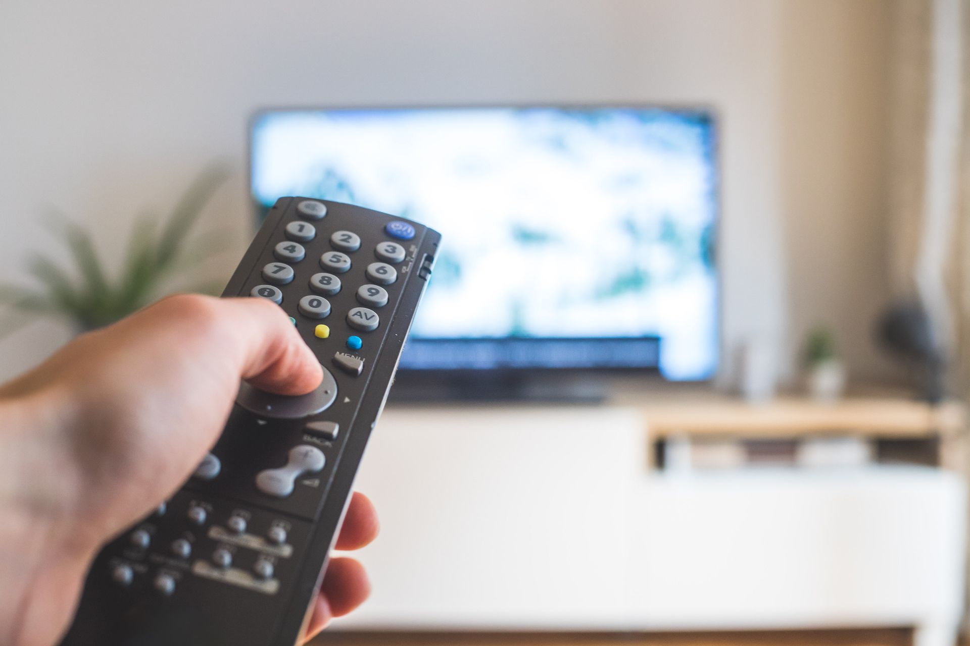 Una persona sostiene un control remoto frente a un televisor.