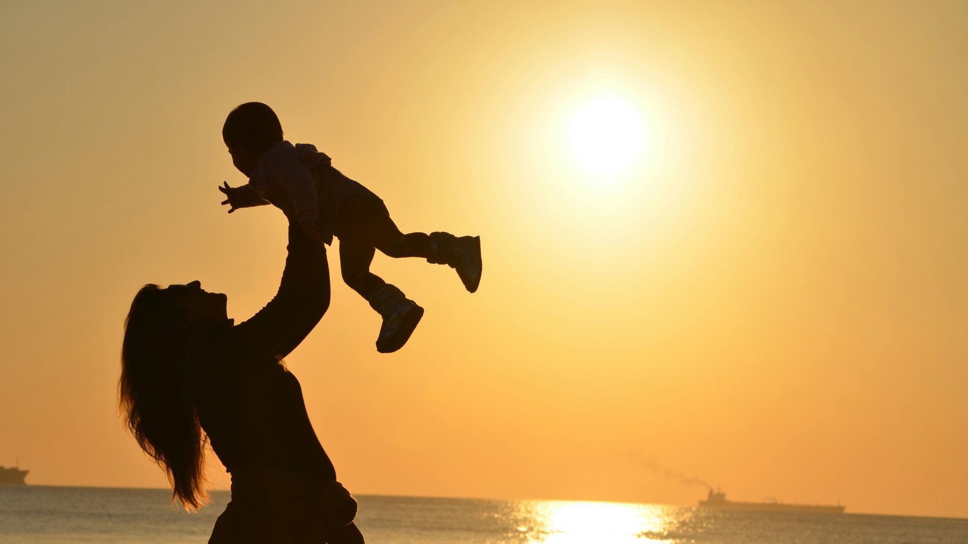 Eine Frau hält bei Sonnenuntergang am Strand ein Baby im Arm.