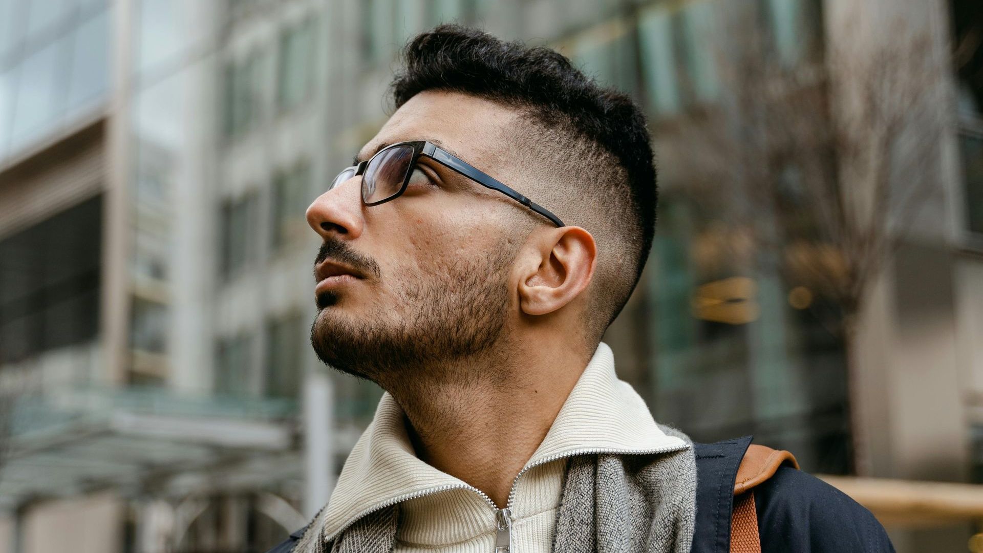Ein Mann mit Brille und Schal steht vor einem Gebäude.