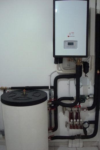 Chaudière et chauffe-eau blancs avec tuyaux et vannes noirs sur un mur blanc.