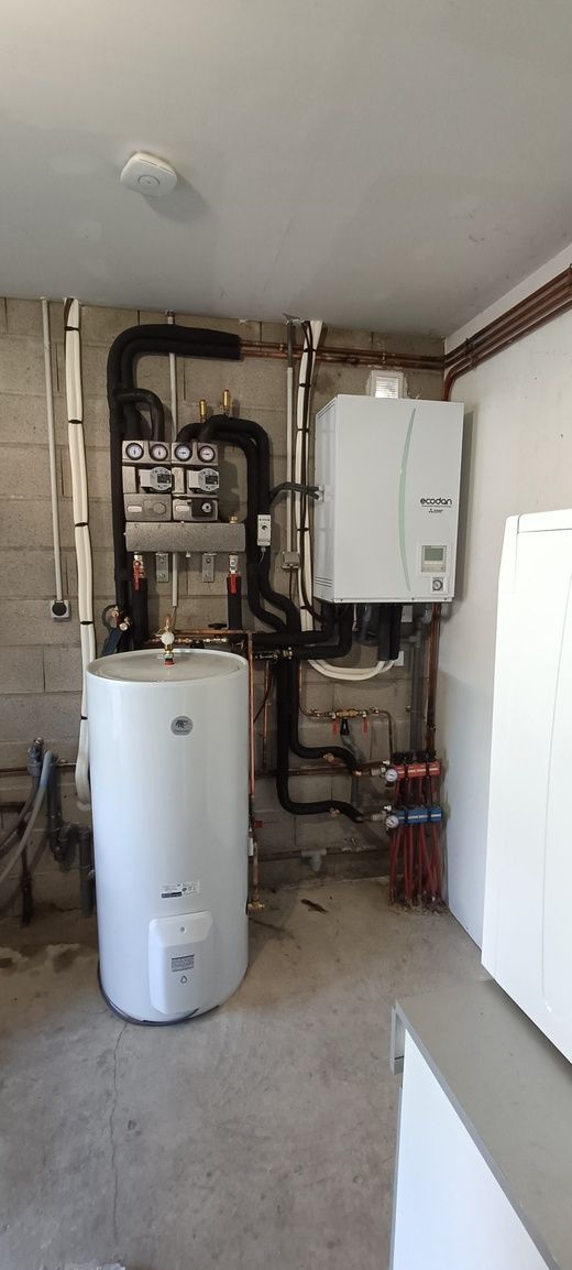 Une buanderie avec un grand chauffe-eau, une chaudière et les canalisations associées.