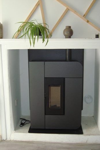 Poêle à granulés gris anthracite dans une niche à cadre blanc, avec une plante et un vase posés dessus.