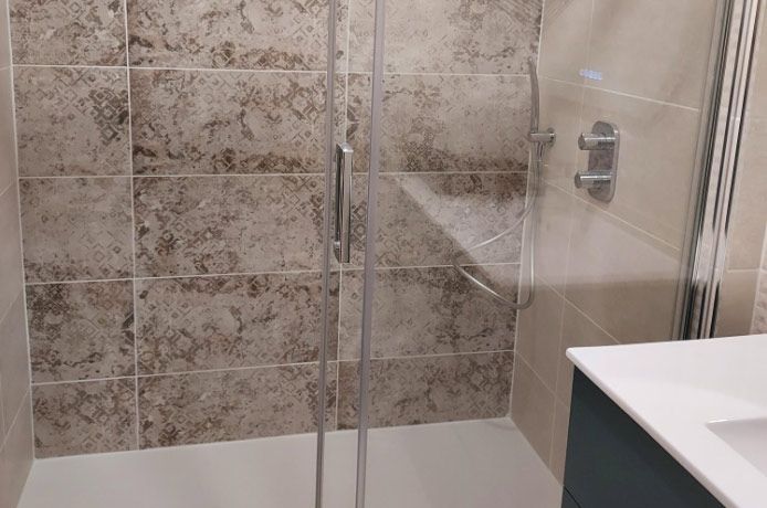 Cabine de douche avec portes en verre, murs carrelés beiges et marron, et sol de douche blanc.