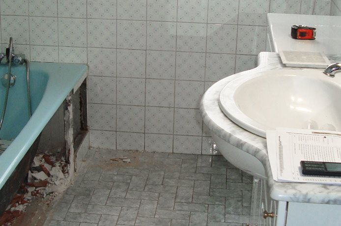 Salle de bains avec baignoire bleue, lavabo et murs et sol carrelés.