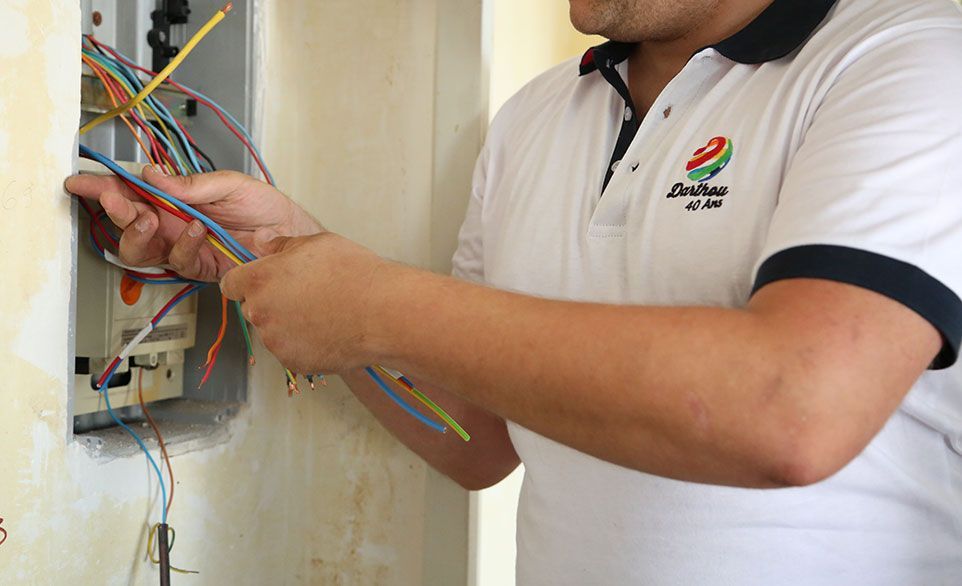 Un électricien travaillant sur le câblage électrique dans une boîte murale, vêtu d'une chemise blanche.