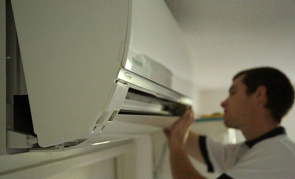 Un homme effectue la maintenance d'un climatiseur mural blanc, en ouvrant un panneau.