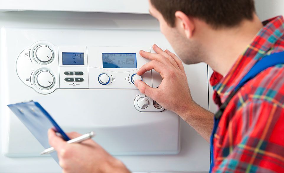 Une personne ajuste les boutons d'une chaudière blanche, tenant un bloc-notes, chemise à carreaux rouges.