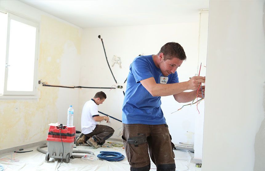 Deux électriciens effectuent le câblage d'une pièce lors d'une rénovation.