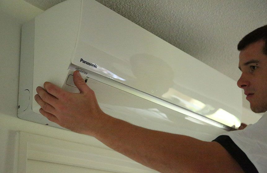 Un homme installe un climatiseur Panasonic blanc sur un mur au-dessus d'une porte.