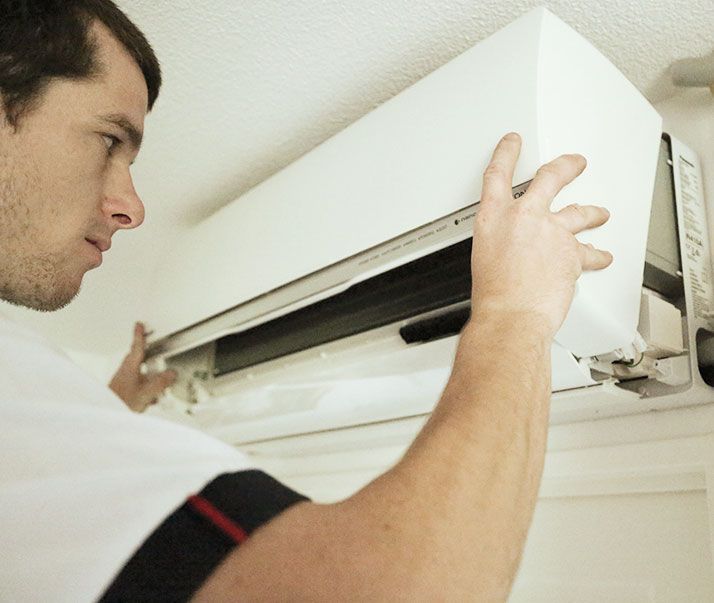Un homme inspecte un climatiseur blanc fixé sur un mur blanc.