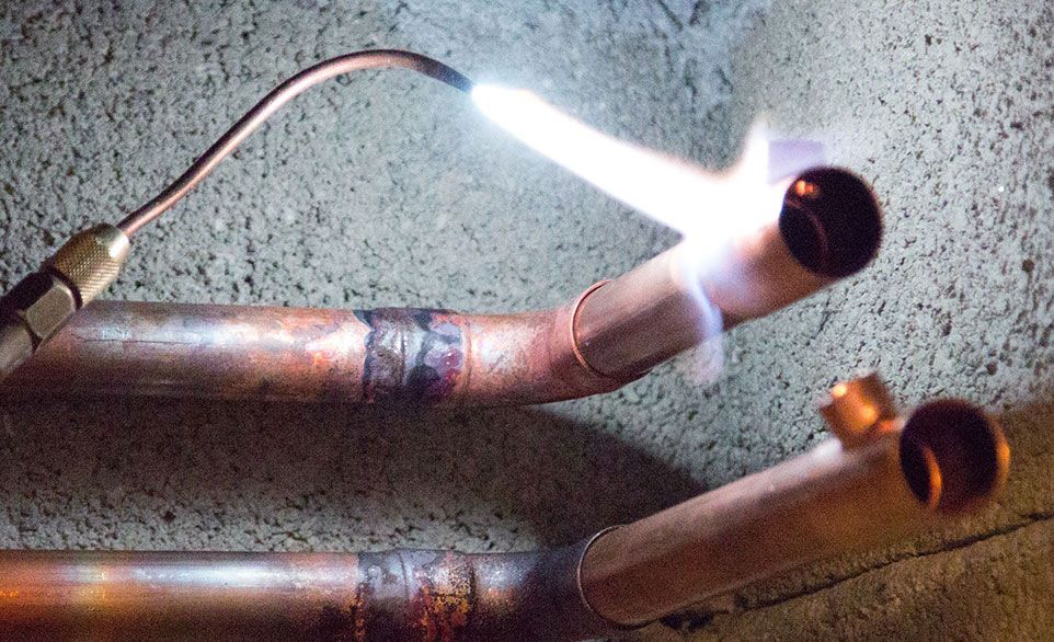 Une personne utilise un chalumeau pour souder des tuyaux de cuivre. Les tuyaux sont en bronze et la flamme est d'un bleu et d'un blanc éclatants.
