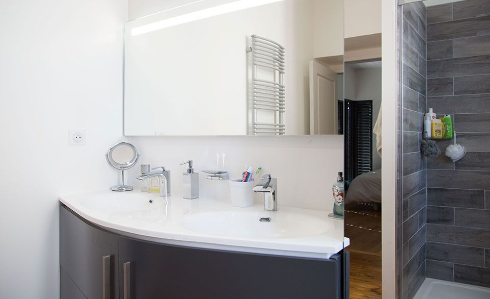 Salle de bains avec meuble-lavabo incurvé, grand miroir et douche carrelée grise.