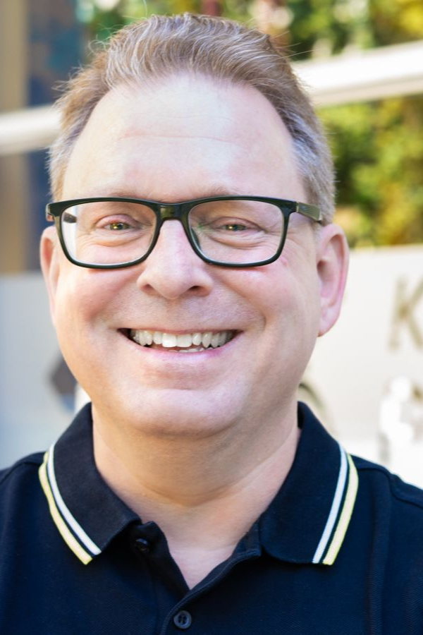 Karl Zeidler, Inhaber der Physiotherapie-Praxis in Aachen-Laurensberg, lächelnd vor dem Praxisschild