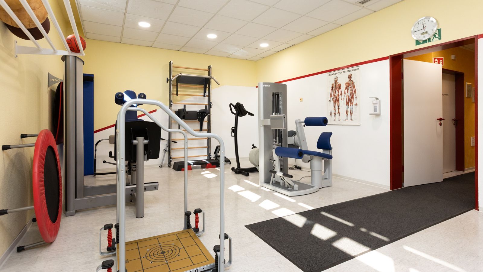 Heller Trainingsbereich der Physiotherapie-Praxis Karl Zeidler in Aachen mit Trampolin, Sprossenwand und Trainingsgeräten für Krankengymnastik