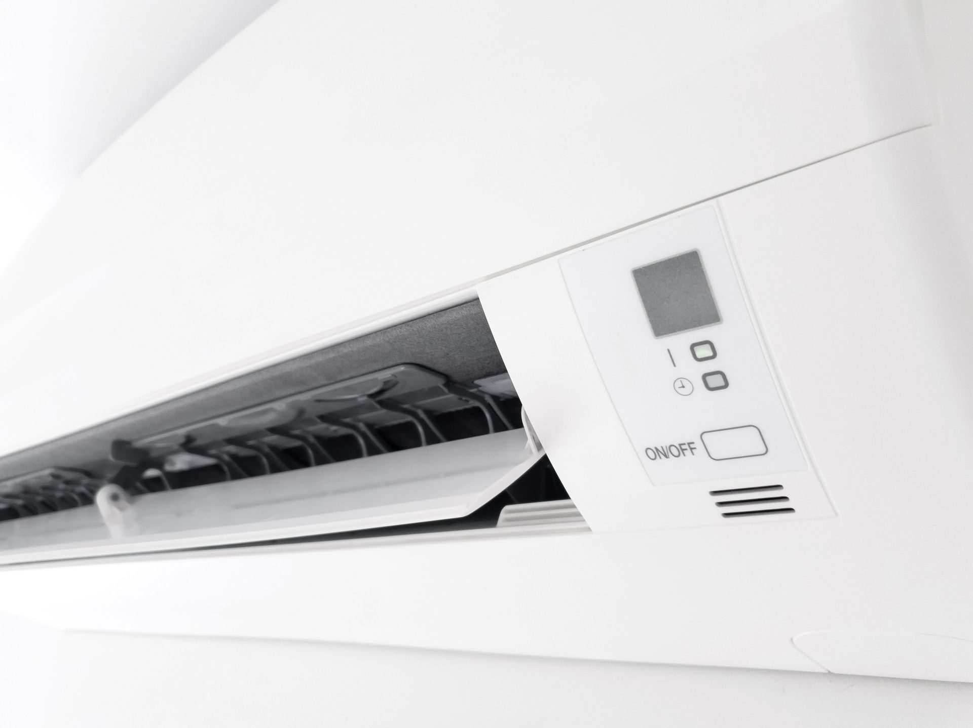 Unité de climatisation blanche fixée au mur, avec grilles d'aération et panneau de commande.