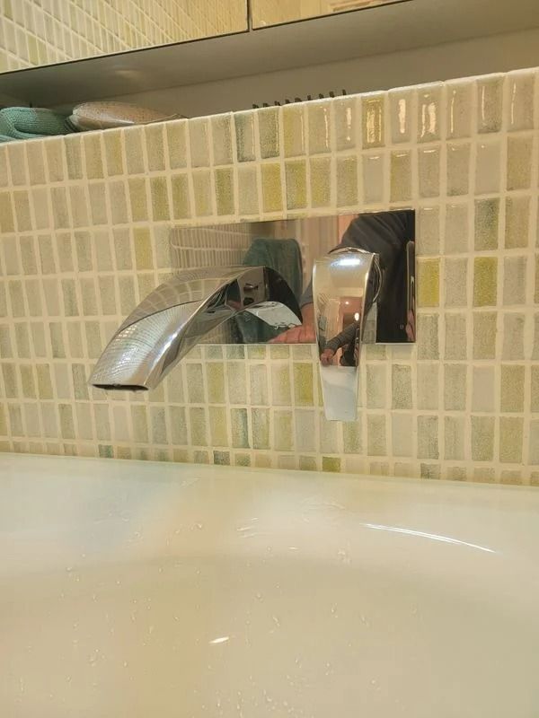 Robinet chromé fixé sur un mur carrelé au-dessus d'un lavabo blanc.